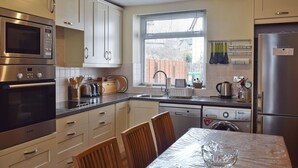 Une cuisine équipée d’appareils électroménagers en acier inoxydable, une fenêtre avec des stores et une table à manger avec des chaises.