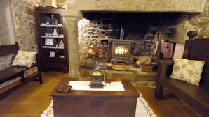 A cozy room with a stone fireplace, wooden furniture, and a traditional stove. - Os Migueliños (Catoira)