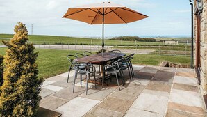 Une terrasse extérieure avec une table et des chaises, un parasol et une vue sur la campagne.