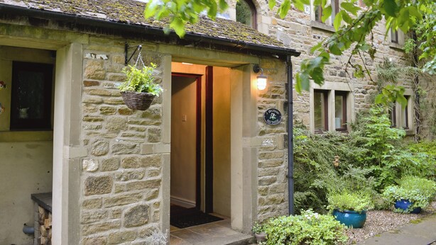 Un bâtiment en pierre avec une porte en bois, un panier suspendu rempli de plantes et une enseigne indiquant « Orchard Cottages ».