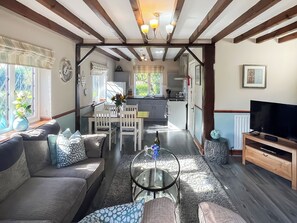 Una sala de estar acogedora con un sofá, una mesa de centro y un televisor. Se ve una cocina al fondo.