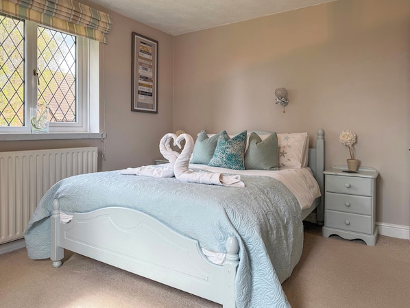 A bedroom with a bed, a nightstand, a framed picture on the wall, and a window with a view.