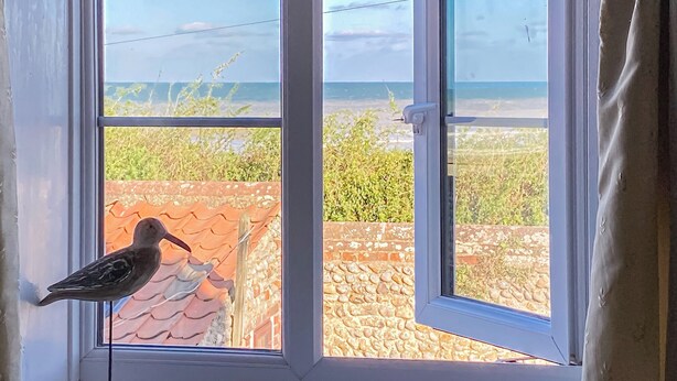 A bird perched on a window sill, with a view of a stone wall and greenery outside. - 2 bedroom accommodation in Bacton (Bacton)