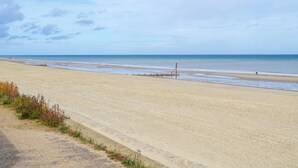 A wide sandy beach with gentle waves, a clear sky, and a lifeguard tower in the distance. - 2 bedroom accommodation in Bacton (Bacton)