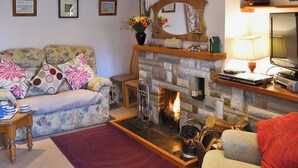 A cozy living room with a stone fireplace, a sofa, a coffee table, and a television. - 2 bedroom accommodation in Bacton (Bacton)
