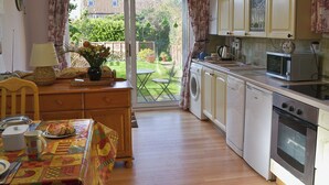 A kitchen with wooden cabinets, a washing machine, a microwave, and a dining area with a table and chairs. - 2 bedroom accommodation in Bacton (Bacton)