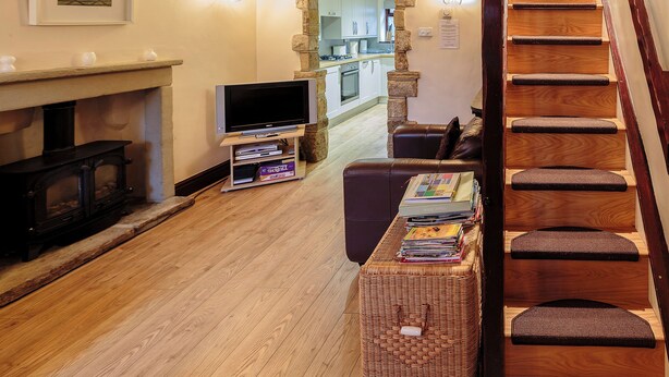 Een woonkamer met een open haard, een televisie, een trap en een keuken op de achtergrond.