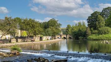 A riverside walkway with benches, a stone bridge, and a calm river.