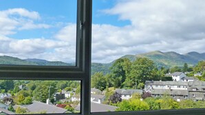 A view through a window of a residential area with houses, greenery, and mountains in the background. - Badgers Rake 12 Squirrels Nest (Ambleside)
