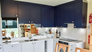 A modern kitchen with dark blue cabinets, white countertops, and a wooden dining table. - Badgers Rake 12 Squirrels Nest (Ambleside)