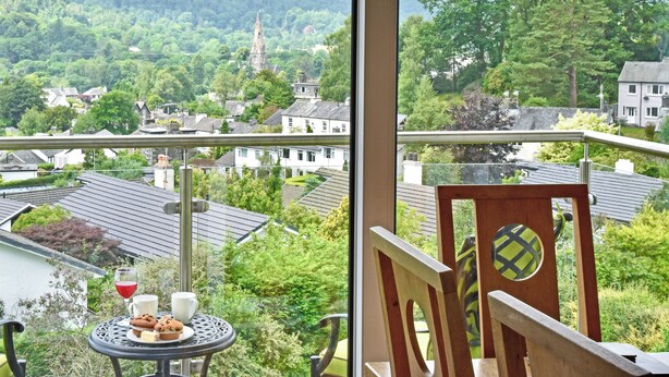 A balcony with a table set for two, overlooking a village with houses and a church. - Badgers Rake 12 Squirrels Nest (Ambleside)