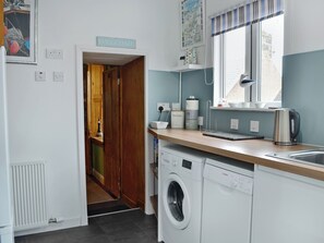 A compact kitchen with a washing machine, a kettle, and a sink.