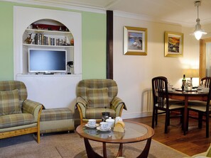 A living room with two armchairs, a coffee table, a bookshelf, a television, and a dining area with chairs and a table.