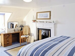 A bedroom with a bed, a desk with a chair, a fireplace, and a framed picture on the wall. - Boatmans Cottage - 27787 (Portessie, near Buckie)