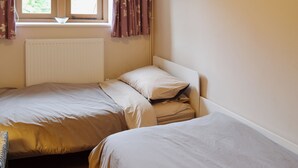 Ein Schlafzimmer mit zwei Einzelbetten, einem Fenster mit Vorhängen, einem Heizkörper und Blick ins Grüne.