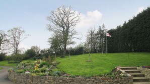 Un mur de pierre avec un parterre de fleurs et un mât de drapeau dans un parc.