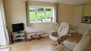 Un salon équipé d’un téléviseur, d’un banc, de deux fauteuils et d’une fenêtre donnant sur l’extérieur.