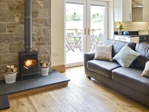 A cozy living room with a stone fireplace, a leather sofa, and a view of the outdoor patio. - 2 bedroom accommodation in Rhostryfan, Caernarfon (Rhostryfan, Caernarfon)