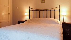 A neatly made bed with a quilted cover, two bedside tables with lamps, and a door to the left.