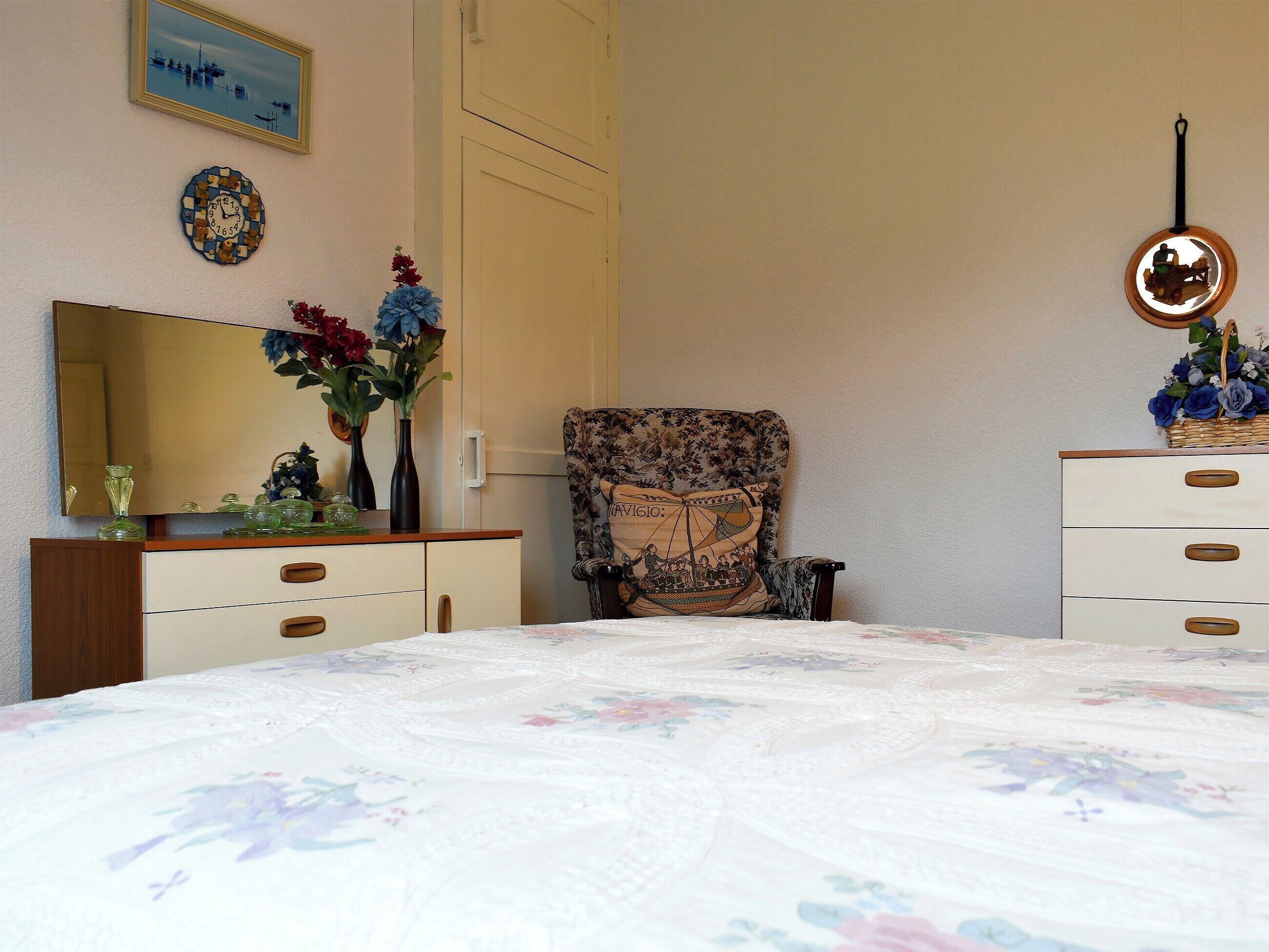 Ein Schlafzimmer mit Bett, Kommode, Stuhl und Spiegel.