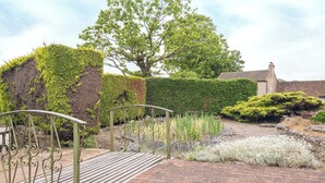 A garden with a metal gate, a brick pathway, and various plants.