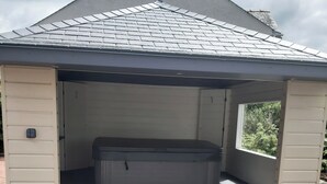 A covered hot tub area with a small step leading up to it, surrounded by beige siding walls and a sloped roof.