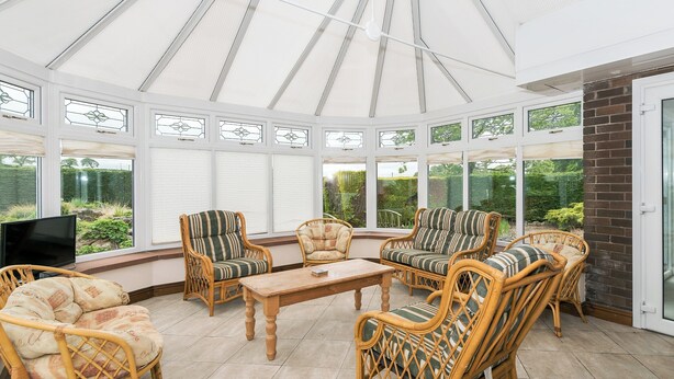 A conservatory with wicker furniture, a wooden table, and a TV on the left.