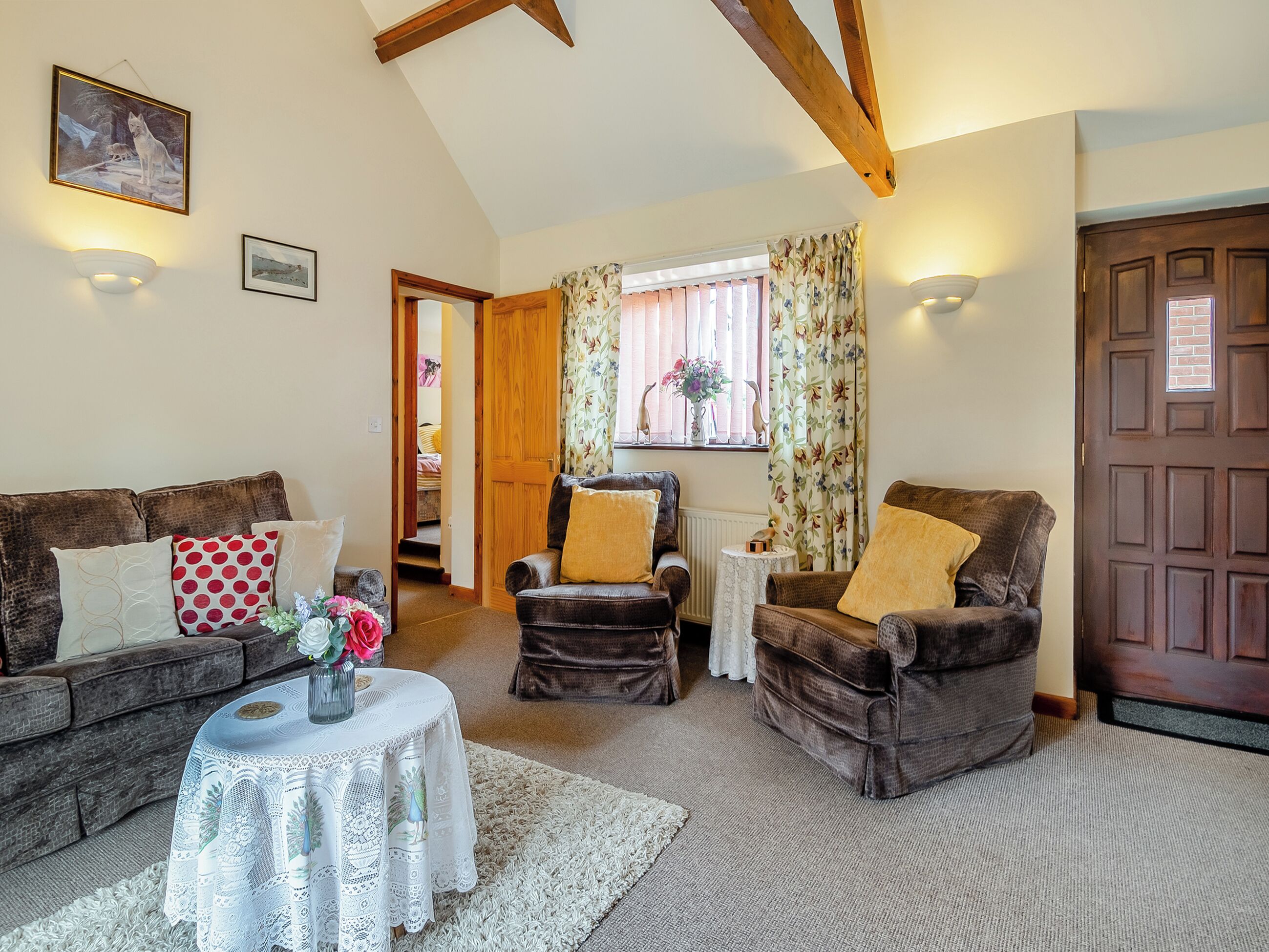 A cozy living room with a brown sofa, a smaller armchair, a white table with a lace tablecloth, and a wooden door.