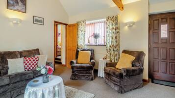 A cozy living room with a brown sofa, a smaller armchair, a white table with a lace tablecloth, and a wooden door.