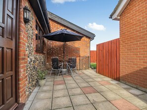 A patio with a brick wall, a wooden door, and a table with chairs under a black umbrella. - 3 bedroom accommodation in Banham (Banham)