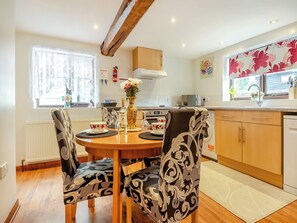 A modern kitchen with wooden cabinets, a dining table with patterned chairs, a vase with flowers, and a microwave. - 3 bedroom accommodation in Banham (Banham)