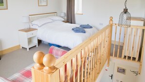 A bedroom with a bed, nightstands, a wooden staircase, and a hanging light fixture.