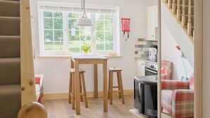 A cozy kitchen with wooden stools, a dining table, a black microwave, and a red plaid chair.