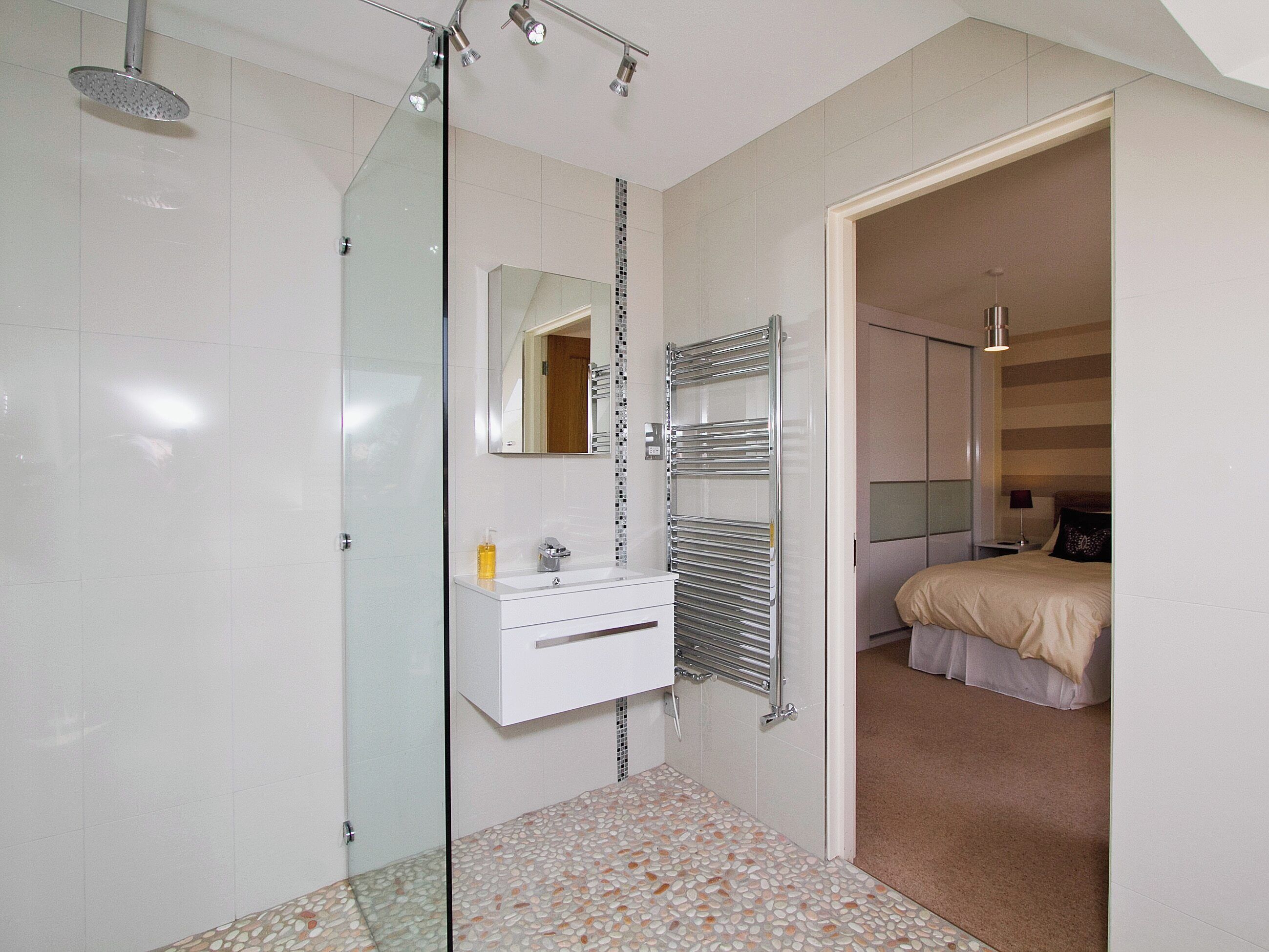 Une salle de bain moderne avec une douche à l’italienne en verre, un meuble-lavabo blanc avec un miroir et un sol carrelé.