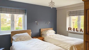 Une chambre avec deux lits simples, une table de chevet avec une lampe et une fenêtre donnant sur l’extérieur.