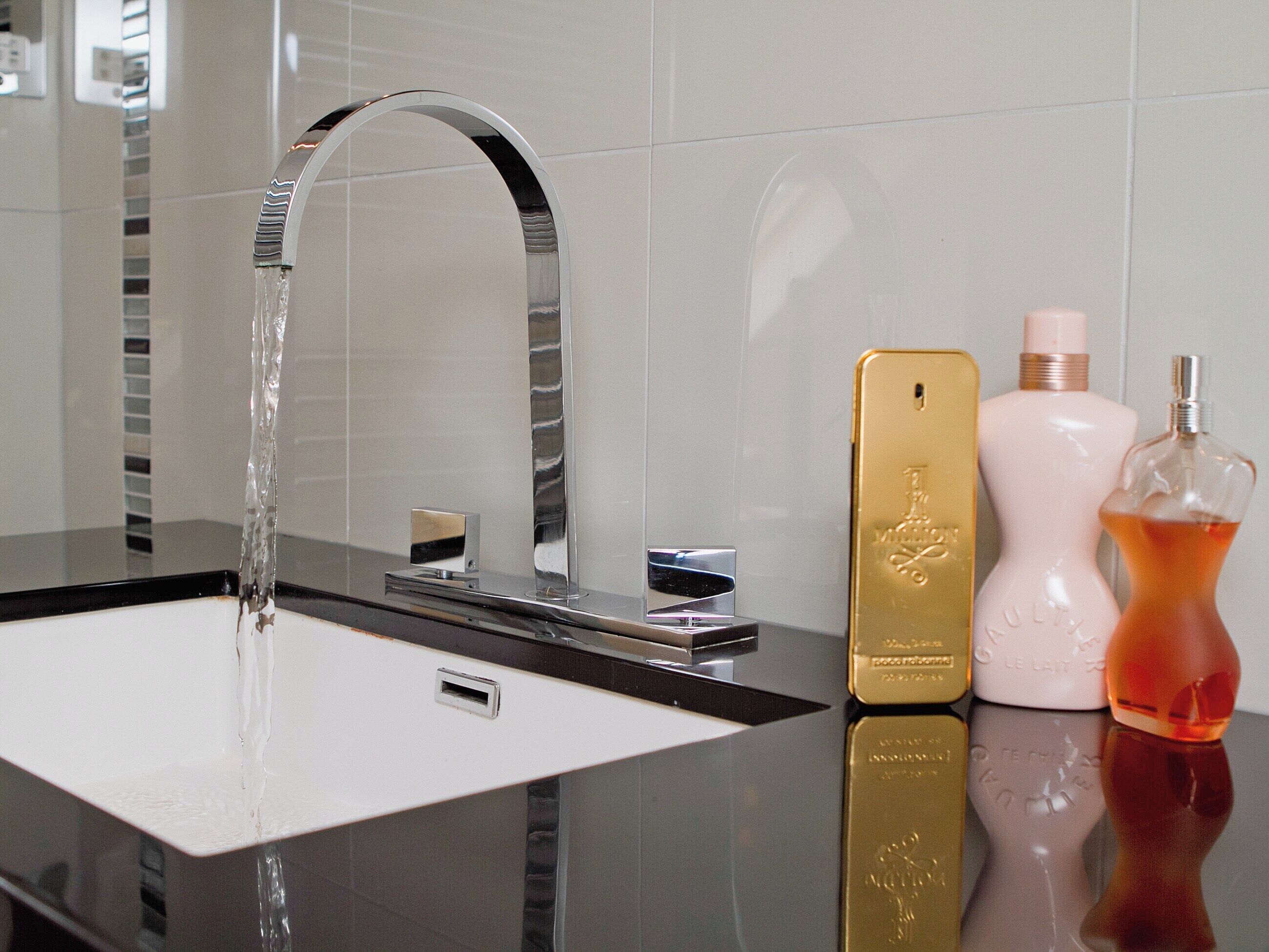 A modern bathroom with a sleek black sink, a chrome faucet, and a mirror. There are three perfume bottles on the counter.