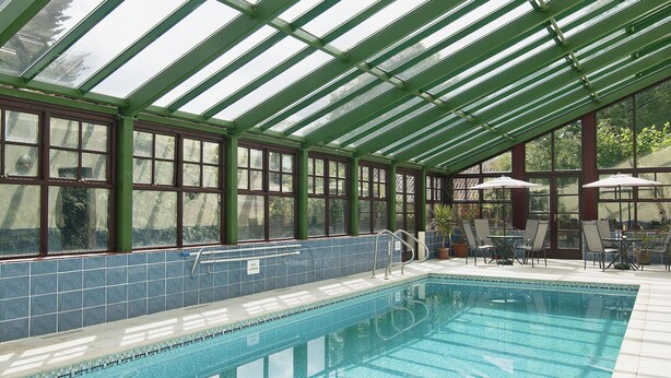 A covered swimming pool with a glass roof, surrounded by chairs and umbrellas, and a tiled pool edge. - 4 bedroom accommodation in Necton, near Swaffham (Necton, near Swaffham)