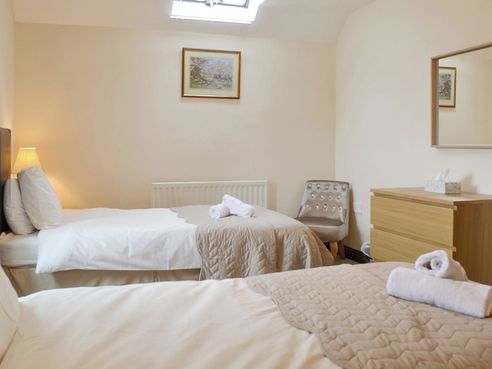 A hotel room with two beds, a chair, a dresser, and a framed picture on the wall.