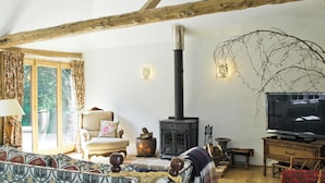 A cozy living room with a high ceiling, a fireplace, a television, and a large window with curtains. - Romantic hideaway for couples (and their pets. (Carlton, near Saxmundham)