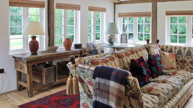A cozy room with a wooden desk, a sofa with floral upholstery, and a red patterned rug. - Romantic hideaway for couples (and their pets. (Carlton, near Saxmundham)