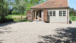 A rustic wooden building with a gravel driveway and a wooden door. - Romantic hideaway for couples (and their pets. (Carlton, near Saxmundham)