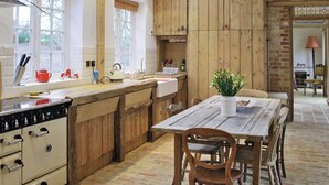 A kitchen with wooden cabinets, a dining table, and a large window. - Romantic hideaway for couples (and their pets. (Carlton, near Saxmundham)