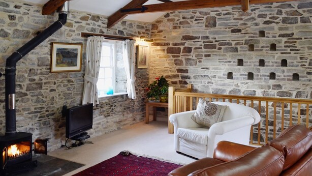 Un salón acogedor con pared de piedra, chimenea, sofá blanco y sillón de cuero.