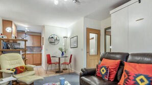 A living room with a leather sofa, a glass coffee table, a beige armchair, and a dining area with a table and chairs. - Short breaks available all year. (Keswick)