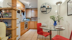 A modern kitchen with wooden cabinets, a glass dining table, red chairs, and a wall-mounted shelf with a clock and decorative items. - Short breaks available all year. (Keswick)