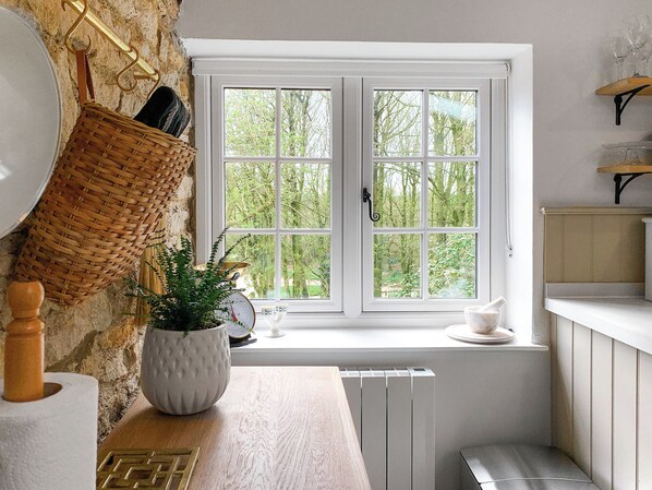Une cuisine avec une fenêtre, un radiateur blanc, un comptoir en bois, un saladier blanc et un panier en osier.