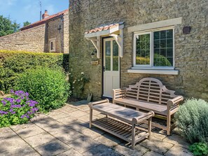A stone cottage with a wooden bench and a door labeled 'Corn Stock.'