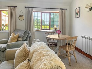Une pièce chaleureuse avec un canapé, une table ronde entourée de chaises, une fenêtre avec des rideaux, un radiateur et une lampe fixée au mur.