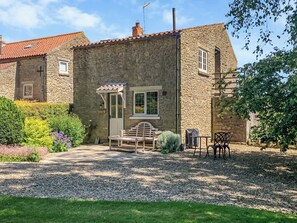 A stone building with a door, windows, and a small patio area with outdoor furniture.