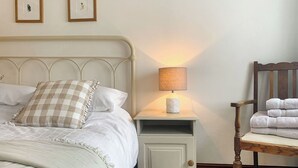 Una cama con cabecera, una mesita de noche con lámpara, una silla con toallas y dos cuadros en la pared.